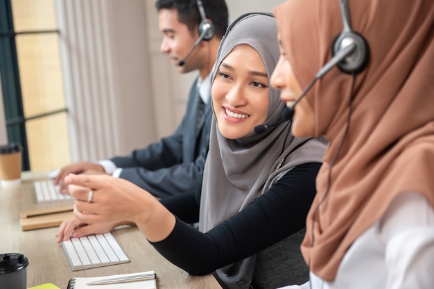 Szczęśliwe piękne Azjatyckie muzułmańskie kobiety pracuje w centrum telefonicznego biurze