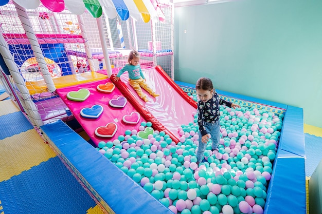 Szczęśliwe siostry bawiące się w krytym centrum zabaw kolorowymi kulkami w basenie z piłeczkami