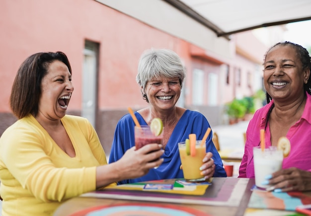 Szczęśliwe starsze koleżanki bawią się razem w mieście, pijąc zdrowe koktajle w barze na świeżym powietrzu