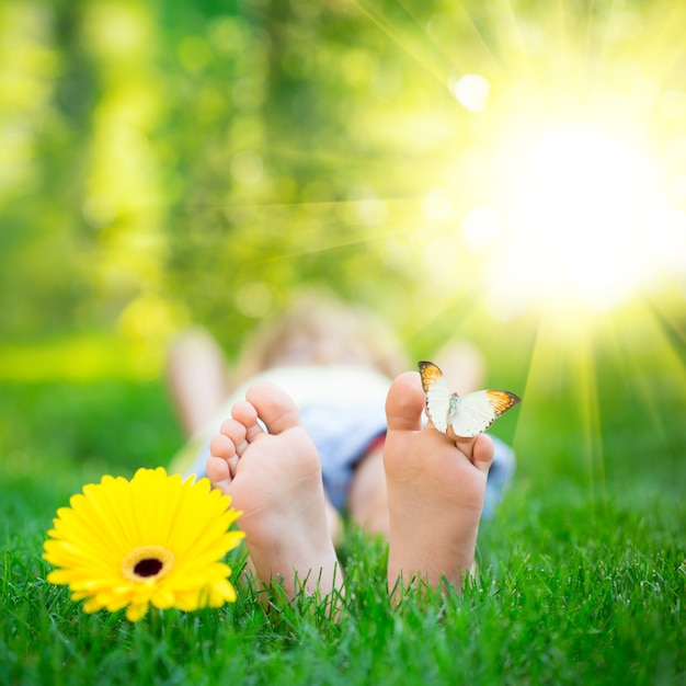 Szczęśliwe stopy z motylem na zewnątrz Dziecko bawiące się w wiosennym parku Dziecko leżące na zielonej trawie