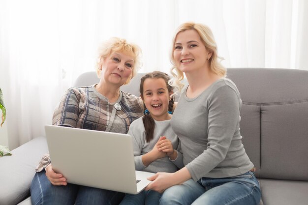 Szczęśliwe Trzy Pokolenia Kobiet Siedzą Odpoczywają Na Kanapie I śmieją Się Oglądając śmieszne Wideo Na Laptopie, Uśmiechnięte Pozytywne Kobiety Babcia, Matka I Córka Bawią Się, Odpoczywają Na Kanapie, Oglądają Film Na Komputerze