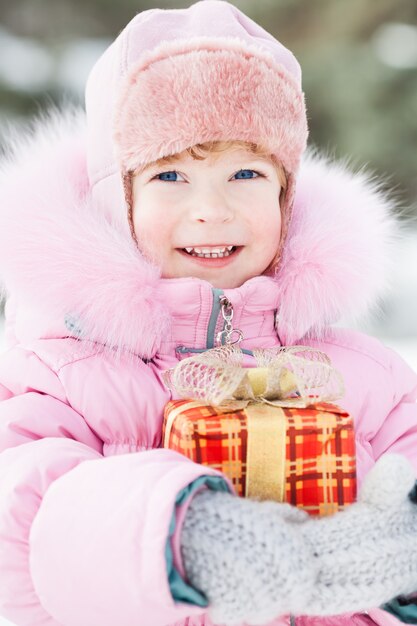 Szczęśliwe uśmiechnięte dziecko z prezentem świątecznym w winter park