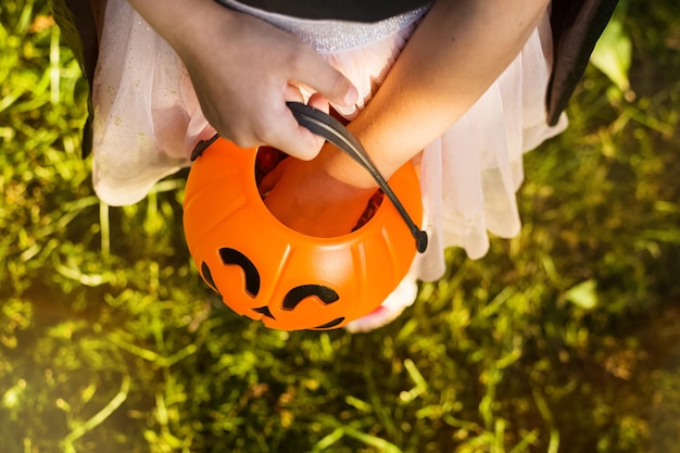 Szczęśliwego dnia Halloween małe dziecko w stroju wiedźmy szuka cukierków w swoim wiaderku z dyni