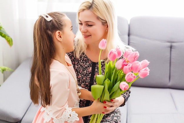 Szczęśliwego dnia Matki. Córka dziecka gratuluje mamie i daje jej kwiaty tulipany. Mama i dziewczyna uśmiechając się i przytulając. Rodzinne wakacje i razem.