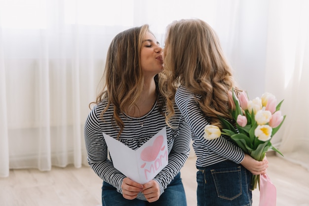 Szczęśliwego Dnia Matki. Córka Dziecka Gratuluje Mamom I Daje Jej Pocztówkę I Kwiaty Tulipanów.