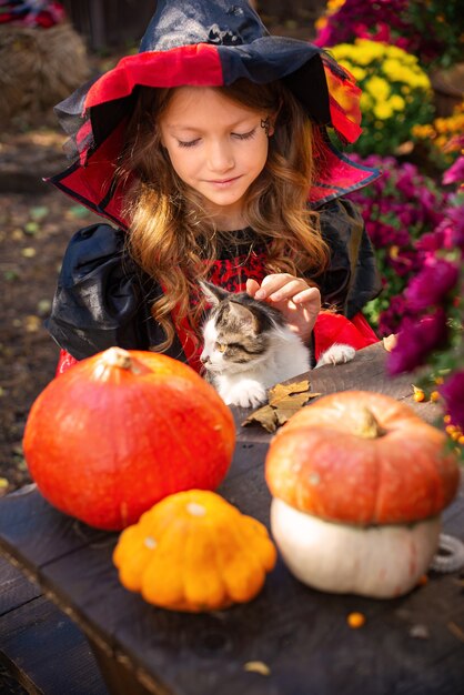 szczęśliwego Halloween dziewczyna w stroju wiedźmy z dynią bawi się jesienią w pobliżu domu