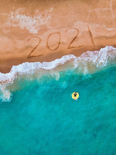 Szczęśliwego Nowego Roku 2021, napis na plaży z falą i błękitnym morzem.