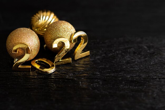 Zdjęcie szczęśliwego nowego roku 2022 złote cyfry czarne tło z drewna złote kule i dekoracje świętują