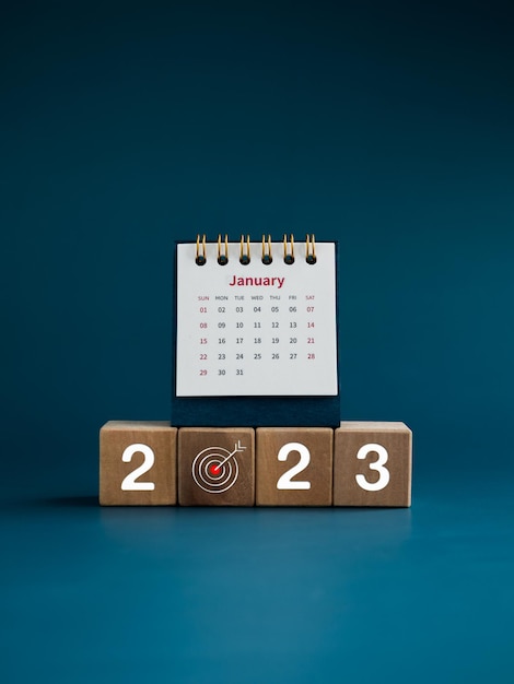 Szczęśliwego Nowego Roku 2023 2023 rok numer z ikoną celu na drewnianych kostkach i mały biały kalendarz biurkowy na stronie stycznia na niebieskim tle pionowym stylu Rozpocznij nowy cel biznesowy do sukcesu