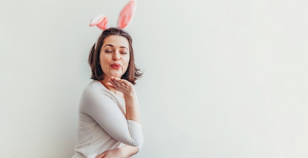 Szczęśliwego Wielkanocnego wakacyjnego świętowania wiosny pojęcie. Młoda kobieta jest ubranym królików ucho odizolowywających na biel ścianie. Przygotowanie do wakacji. Dziewczyna szuka szczęśliwy i podekscytowany zabawy na Wielkanoc. Transparent