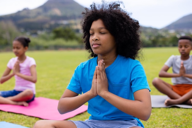 Szczęśliwi afroamerykańscy uczniowie robiący jogę i medytujący na boisku w szkole