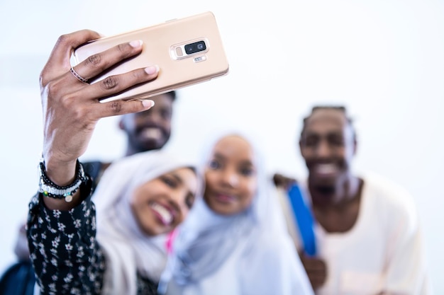 szczęśliwi afrykańscy studenci robiący zdjęcie selfie stojąc razem na białym tle dziewczyny noszące tradycyjny sudański muzułmański hidżab