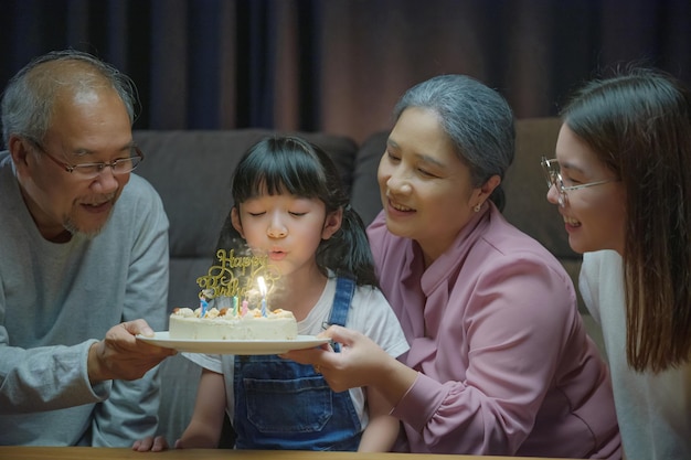 Szczęśliwi azjatyccy dziadkowie i matka świętują przyjęcie urodzinowe z ciastem wnuczki Dmuchanie świeczki w domu w nocy, koncepcja niespodzianki urodzinowej