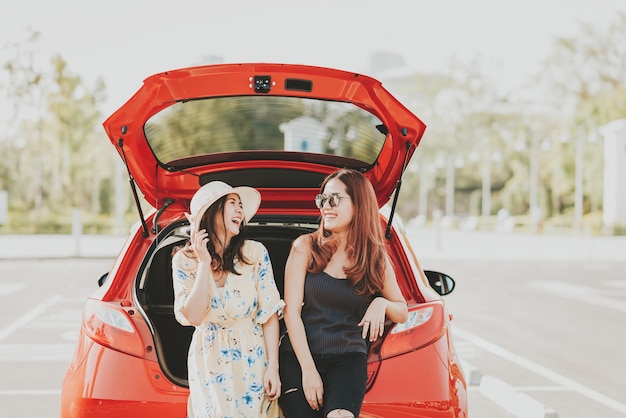 Szczęśliwi Azjatyccy dziewczyna najlepsi przyjaciele śmieją się wpólnie i uśmiechają się podczas gdy siedzący w samochodowym bagażniku