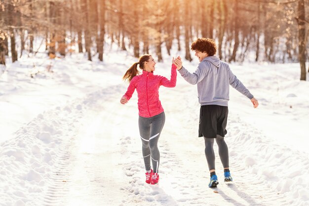 Szczęśliwi biegacze rasy białej, którzy dają piątkę podczas biegania w chłodne dni. Cały śnieg, zima.