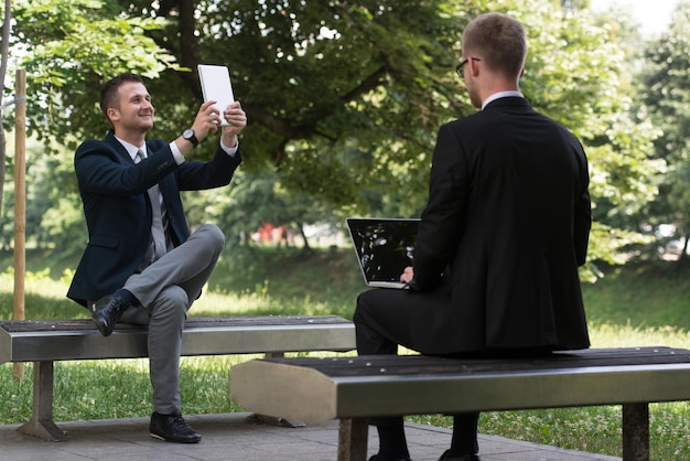 Szczęśliwi biznesmeni korzystający z tabletu na zewnątrz na ławce w parku