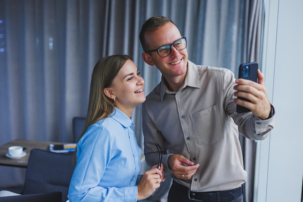 Szczęśliwi koledzy z pracy współpracujący w biurze i korzystający z telefonu Koledzy robią sobie selfie podczas przerwy