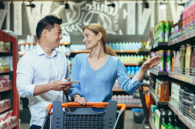 Szczęśliwi kupujący azjatycki mężczyzna i kobieta kupują i wybierają towary w rodzinnych zakupach w supermarkecie