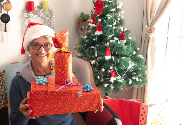 Zdjęcie szczęśliwi ludzie posiadający prezenty świąteczne. choinka na tle. starsza kobieta w czapce mikołaja i uśmiechach