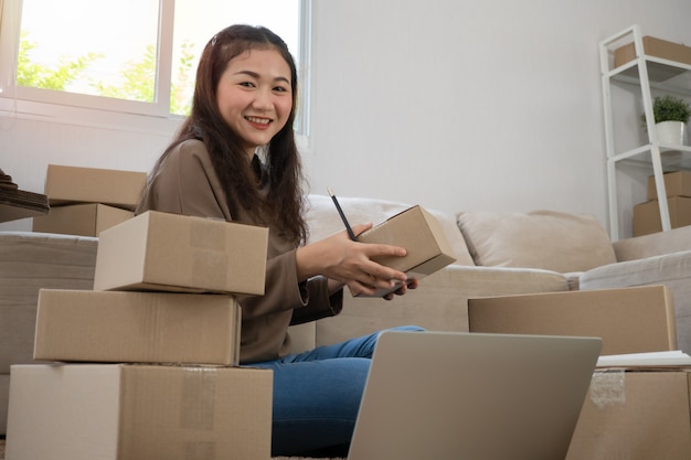 Szczęśliwi młodzi azjatyccy przedsiębiorcy układają pudełka do dostarczania produktów klientom.