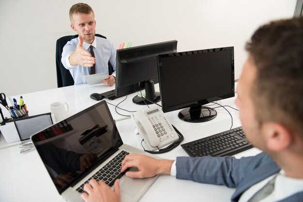 Szczęśliwi młodzi biznesmeni pracują w nowoczesnym biurze na komputerze