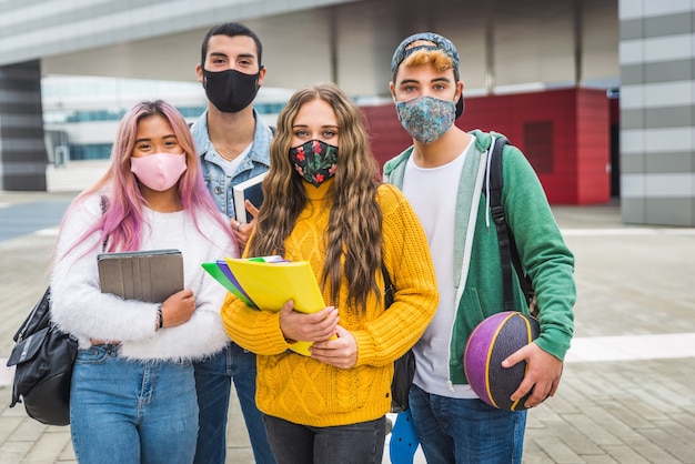 Szczęśliwi młodzi ludzie spotykający się na świeżym powietrzu i noszący maski na twarz podczas pandemii COVID19
