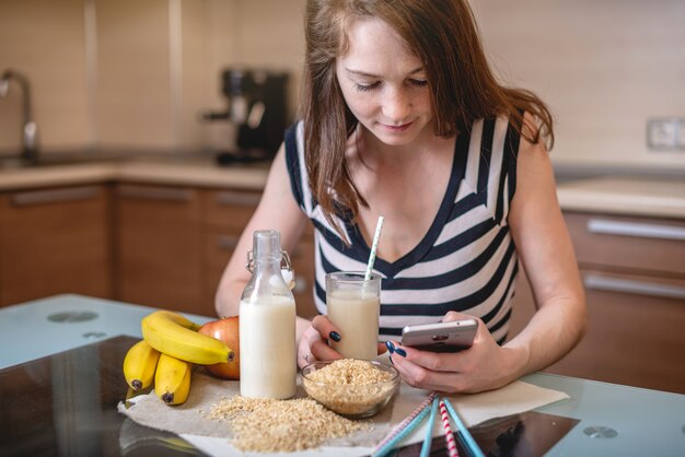 Szczęśliwi Młodzi Pije Organicznie Ryżowy Mleko Podczas Gdy Trzymający Telefon W Kuchni. Dieta Zdrowa Wegetariańska