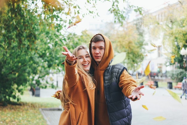 Szczęśliwi potomstwa dobierają się w miłość nastolatków przyjaciółmi ubierających w przypadkowym stylu chodzi wpólnie i rzuca liście przy kamerą, jesieni miasta ulica