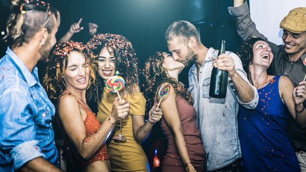 Szczęśliwi przyjaciele bawią się wielorasowo podczas sylwestra - Młodzi ludzie piją i tańczą na after party w nocnym klubie - Koncepcja przyjaźni na pijackim nastroju - Skup się na kobiecie z żółtego materiału