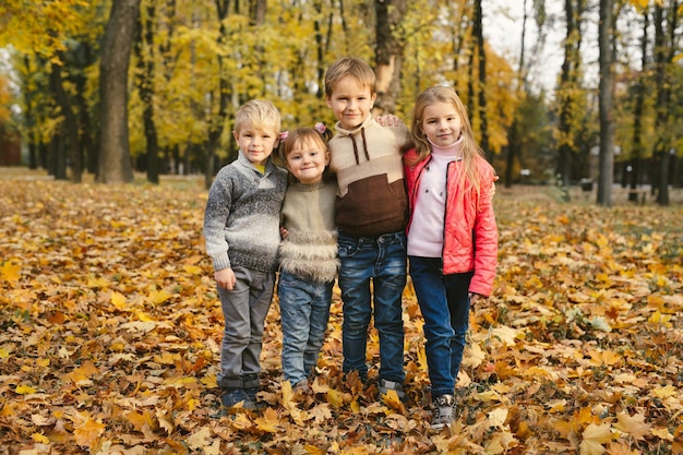 Szczęśliwi przyjaciele dzieci bawią się w jesiennym parku wśród opadłych liści