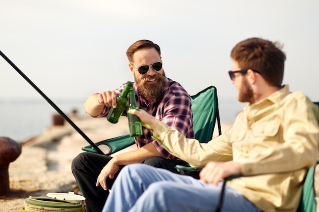 Szczęśliwi przyjaciele łowią ryby i piją piwo na nabrzeżu.