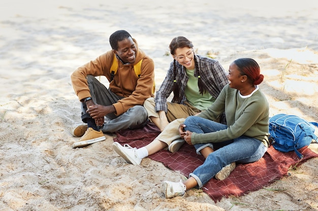 Szczęśliwi przyjaciele siedzą razem na piaskach i cieszą się piknikiem na wybrzeżu