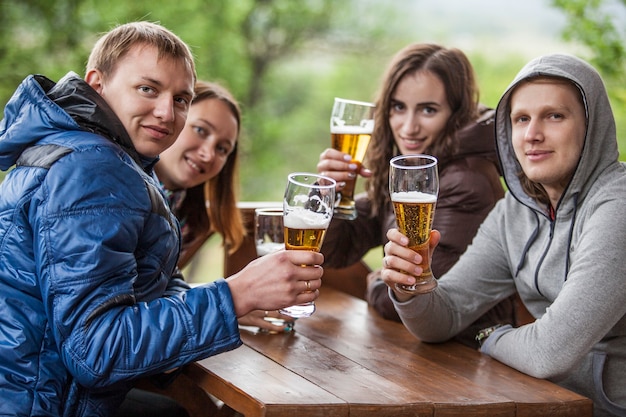 Szczęśliwi przyjaciele siedzą z wysokimi szklankami piwa w ręku przy drewnianym stole