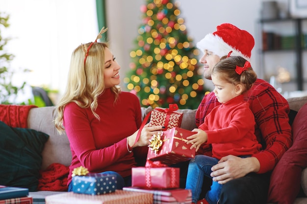 Szczęśliwi rodzice rodzinni i córka dziecka otwierają prezenty w świąteczny poranek
