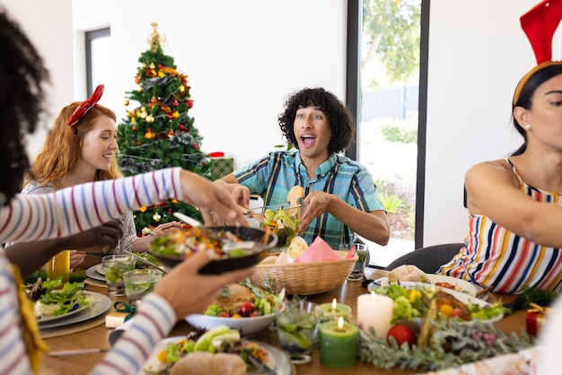 Szczęśliwi, różnorodni przyjaciele siedzący przy stole i jedzący kolację na Boże Narodzenie