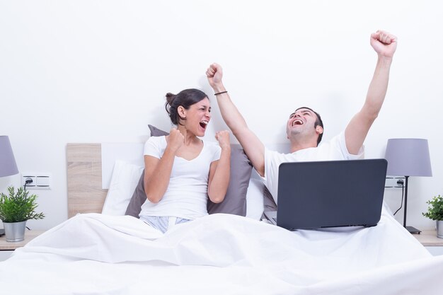 Szczęśliwi śmia się zrelaksowani potomstwa dobierają się używać laptop w łóżku w domu