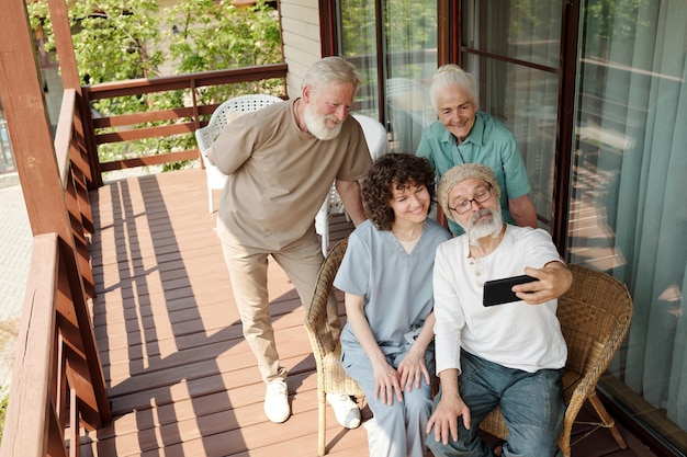 Szczęśliwi starzy ludzie i ich opiekun robią sobie selfie na patio domu opieki