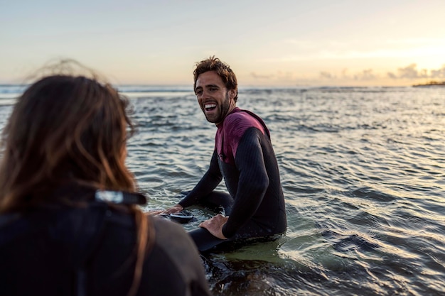 Szczęśliwi surferzy śmieją się ze siebie, siedząc na deskach w wodzie.