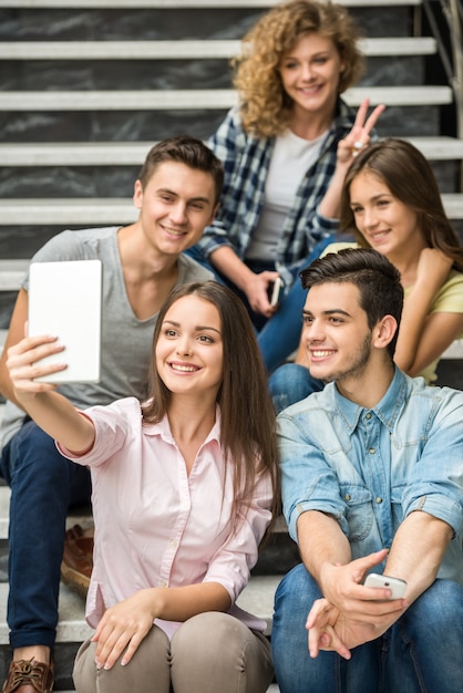 Szczęśliwi uczniowie siedząc na schodach i biorąc selfie.
