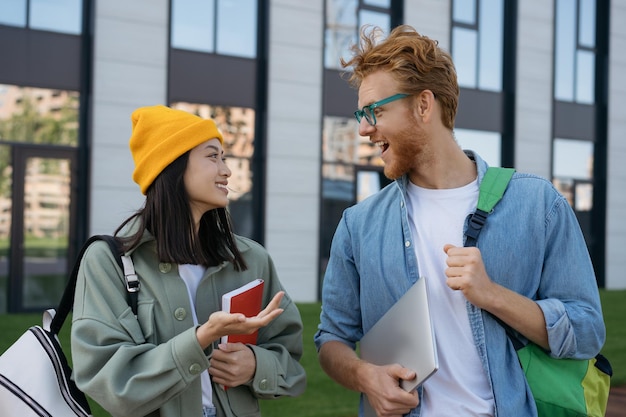 Zdjęcie szczęśliwi wielorasowi studenci z książkami i plecakami w kampusie uniwersyteckim rozmawiają o koncepcji edukacji