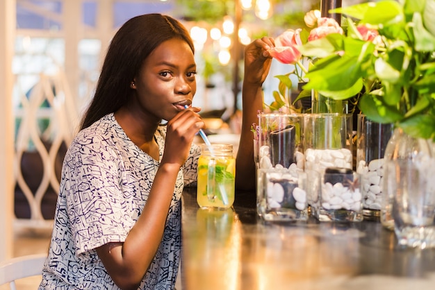 Szczęśliwy African-American kobieta ze szklanką naturalnej lemoniady w kawiarni. Napój detoksykacyjny