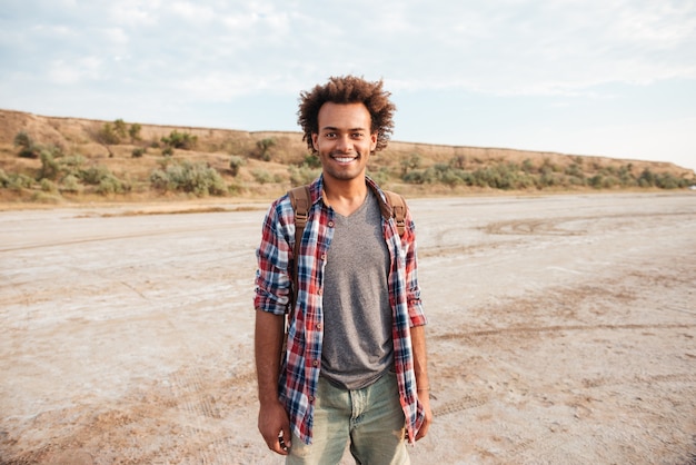 Szczęśliwy afroamerykanin młody człowiek z plecakiem stojący na zewnątrz