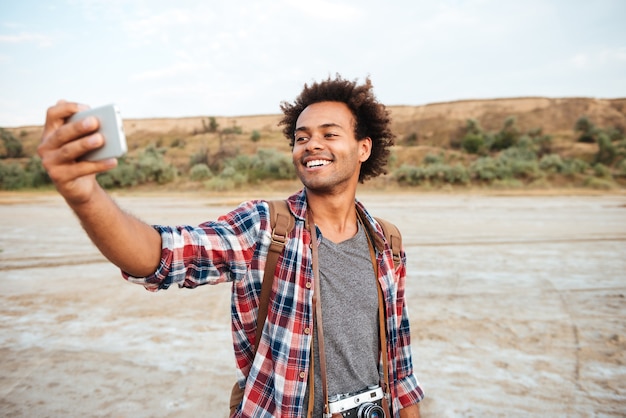Szczęśliwy afroamerykanin stojący i biorący selfie z telefonem komórkowym na zewnątrz