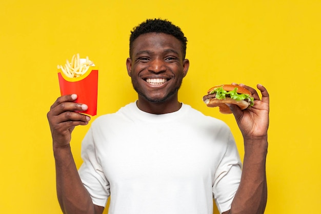 Szczęśliwy Afroamerykanin w białej koszulce trzymający duży burger i frytki i uśmiechający się