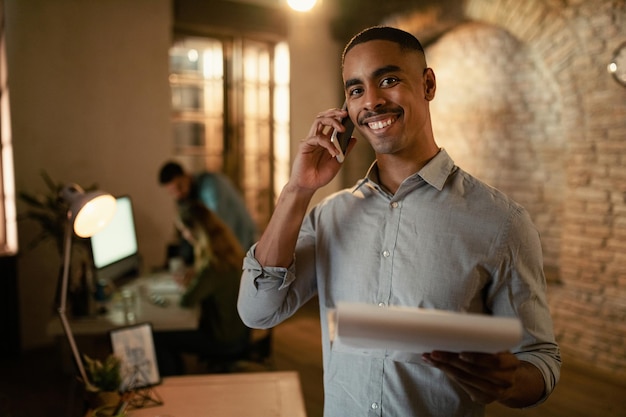 Szczęśliwy Afroamerykański Przedsiębiorca Rozmawia Przez Telefon Komórkowy Podczas Pracy Do Późna W Biurze