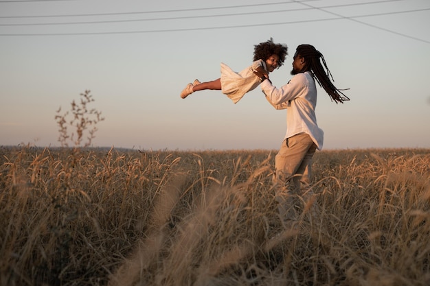 Szczęśliwy afrykański ojciec kręci córkę w ramionach na polu.