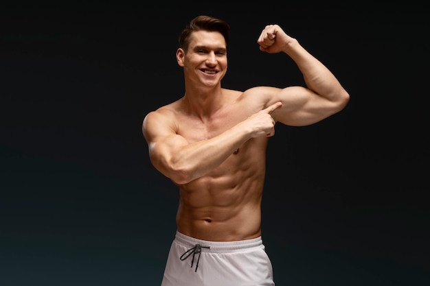 Szczęśliwy atletyczny model demonstrujący bicepsy podczas pozowania z nagim torsem