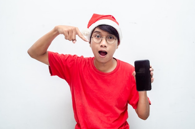 szczęśliwy atrakcyjny azjatycki człowiek w czerwonych świątecznych ubraniach tematycznych zszokowany szczęśliwie trzymając telefon.