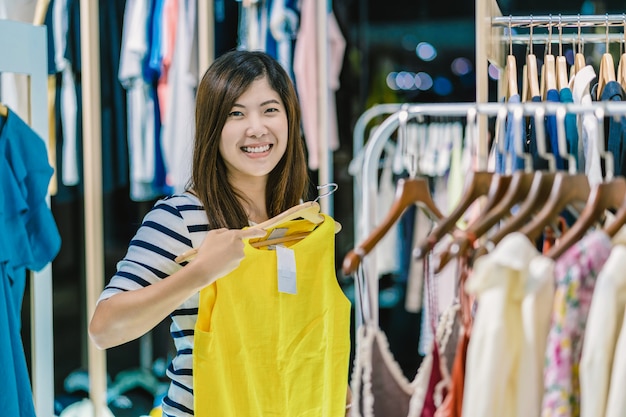 Szczęśliwy Azjatycki kobiety wybierać odziewa w sklepie robi zakupy z szczęśliwą akcją przy wydziałowym centrum