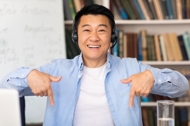 Szczęśliwy azjatycki nauczyciel nosi zestaw słuchawkowy w nowoczesnej bibliotece